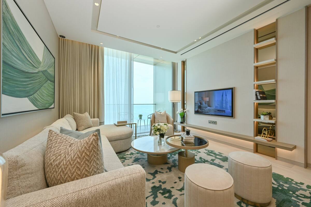 A modern living room with a sofa, coffee table, and ottoman, a TV mounted on the wall, and a bookshelf with decorative items.