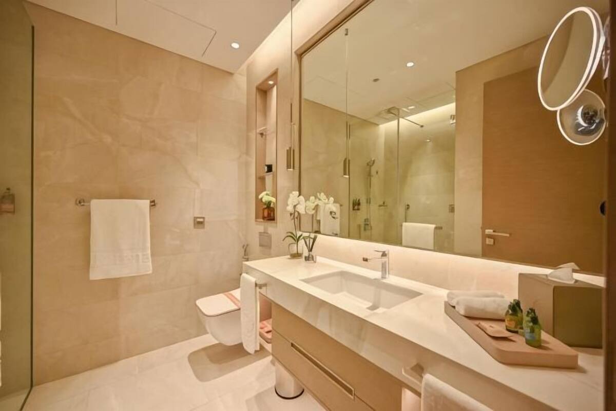 A modern bathroom with a large mirror, two sinks, a toilet, and a vanity with a towel rack.