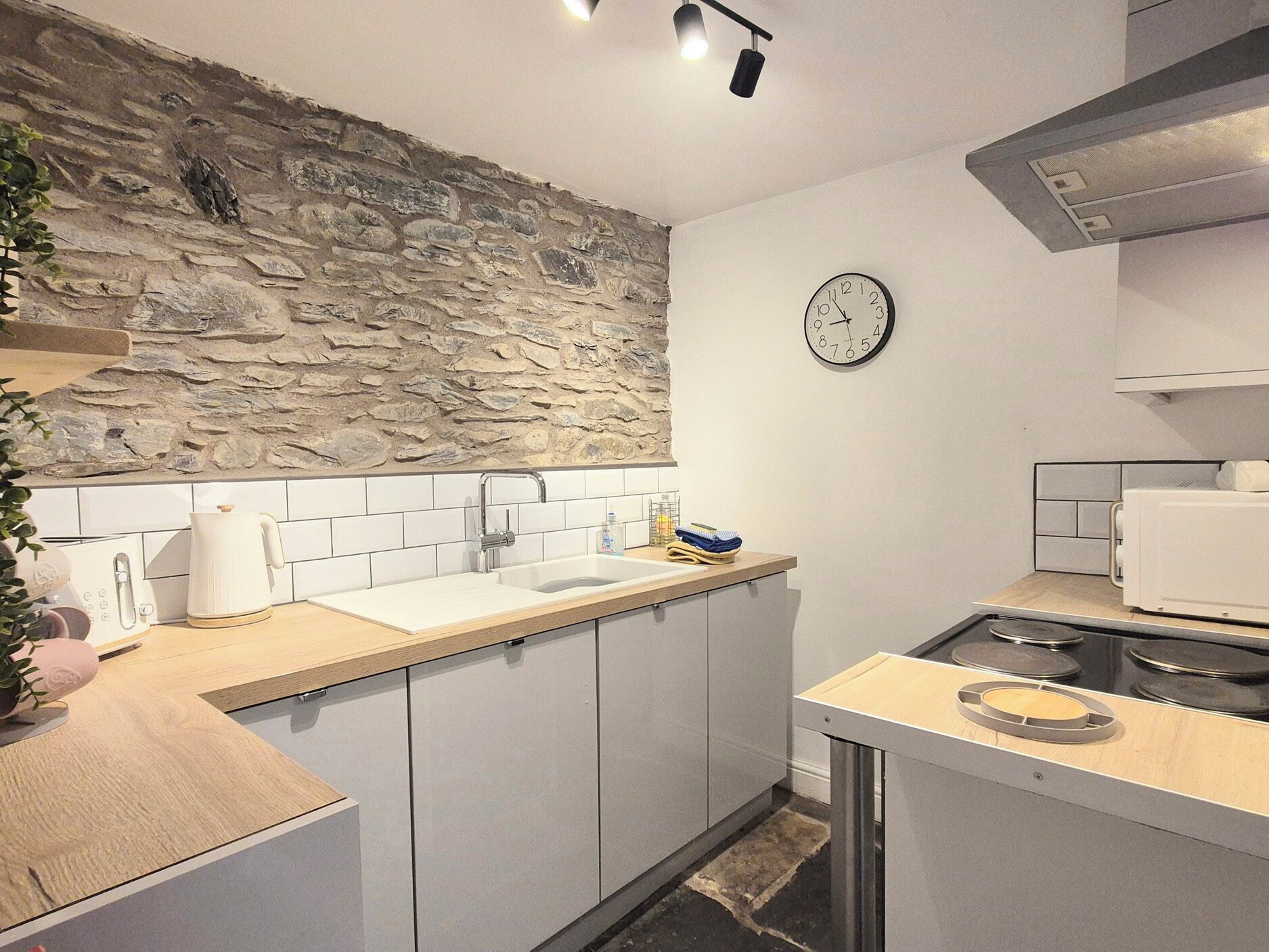 Une cuisine moderne avec un mur de pierre derrière l’évier, un évier, une horloge et une cuisinière.
