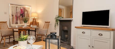 A living room with a fireplace, a television, a dining table with chairs, and a painting on the wall.
