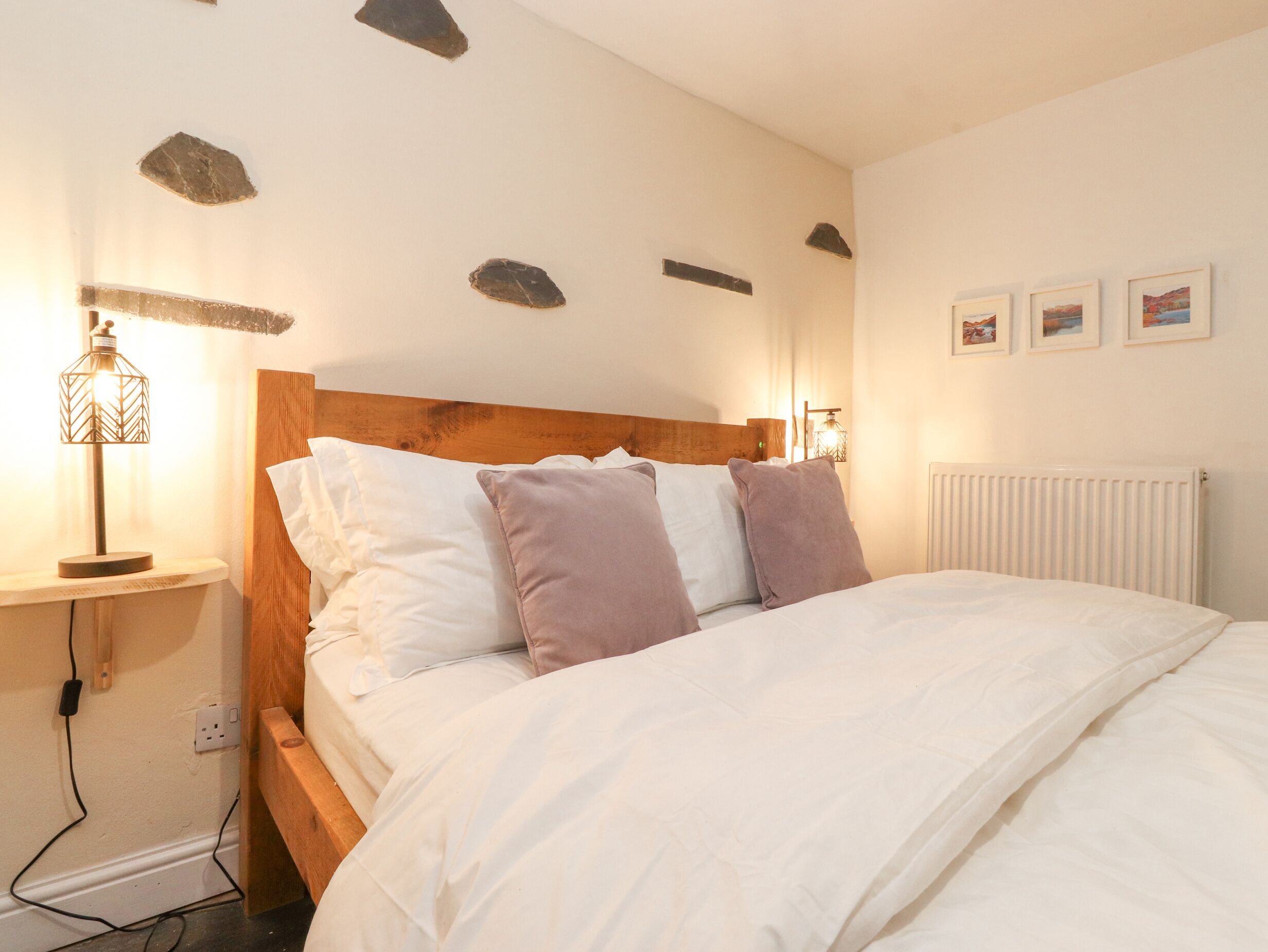 Un lit bien fait, avec des oreillers blancs et violets, une tête de lit en bois et une lampe de chevet.