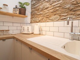 Uma cozinha com painel de backsplash de pedra, azulejos brancos, bancada de madeira, pia, chaleira, torradeira e um letreiro na prateleira.