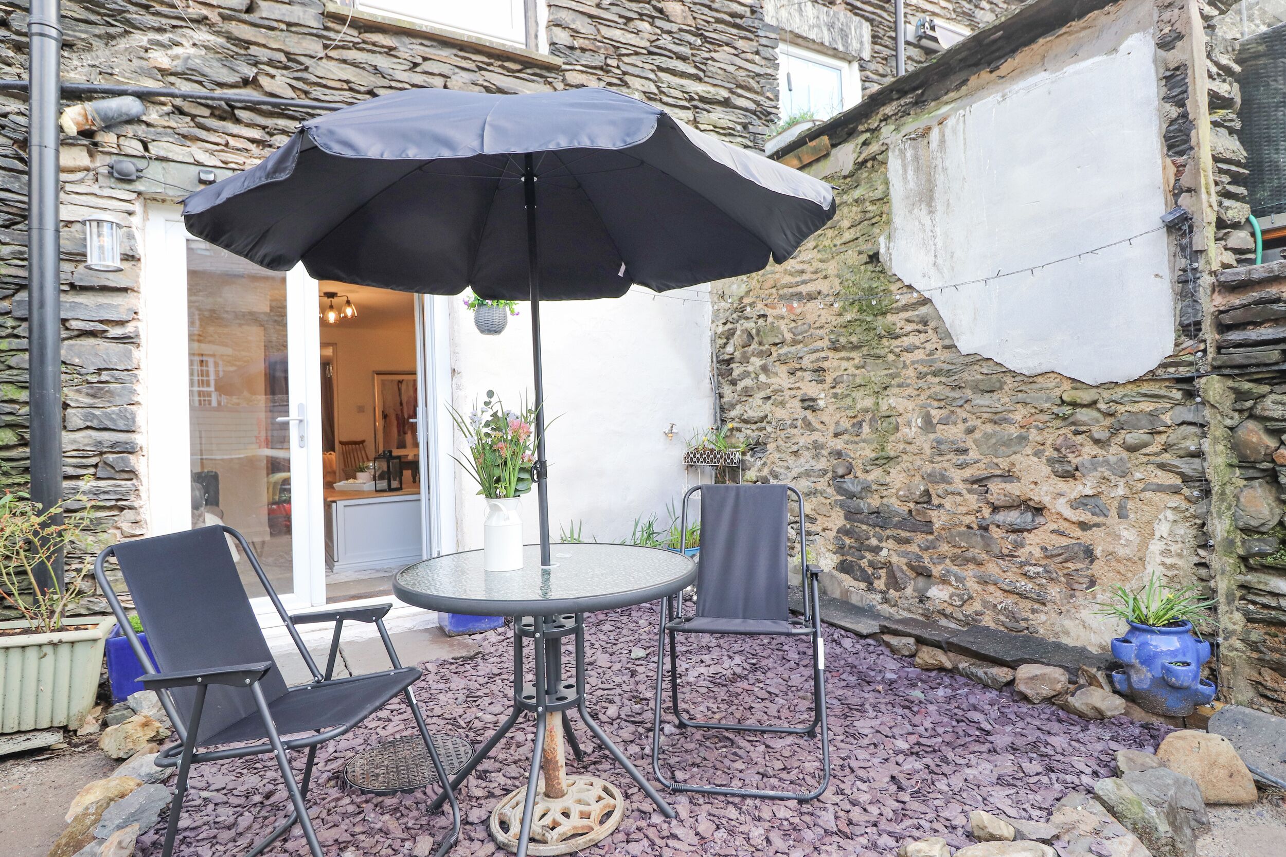 An outdoor seating area with a round table, two chairs, and a large umbrella.