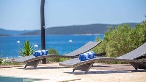 Ett område vid poolen med solstolar och utsikt över havet.