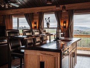 Un intérieur en bois avec un coin bar, des fauteuils en cuir et une vue sur l’extérieur.