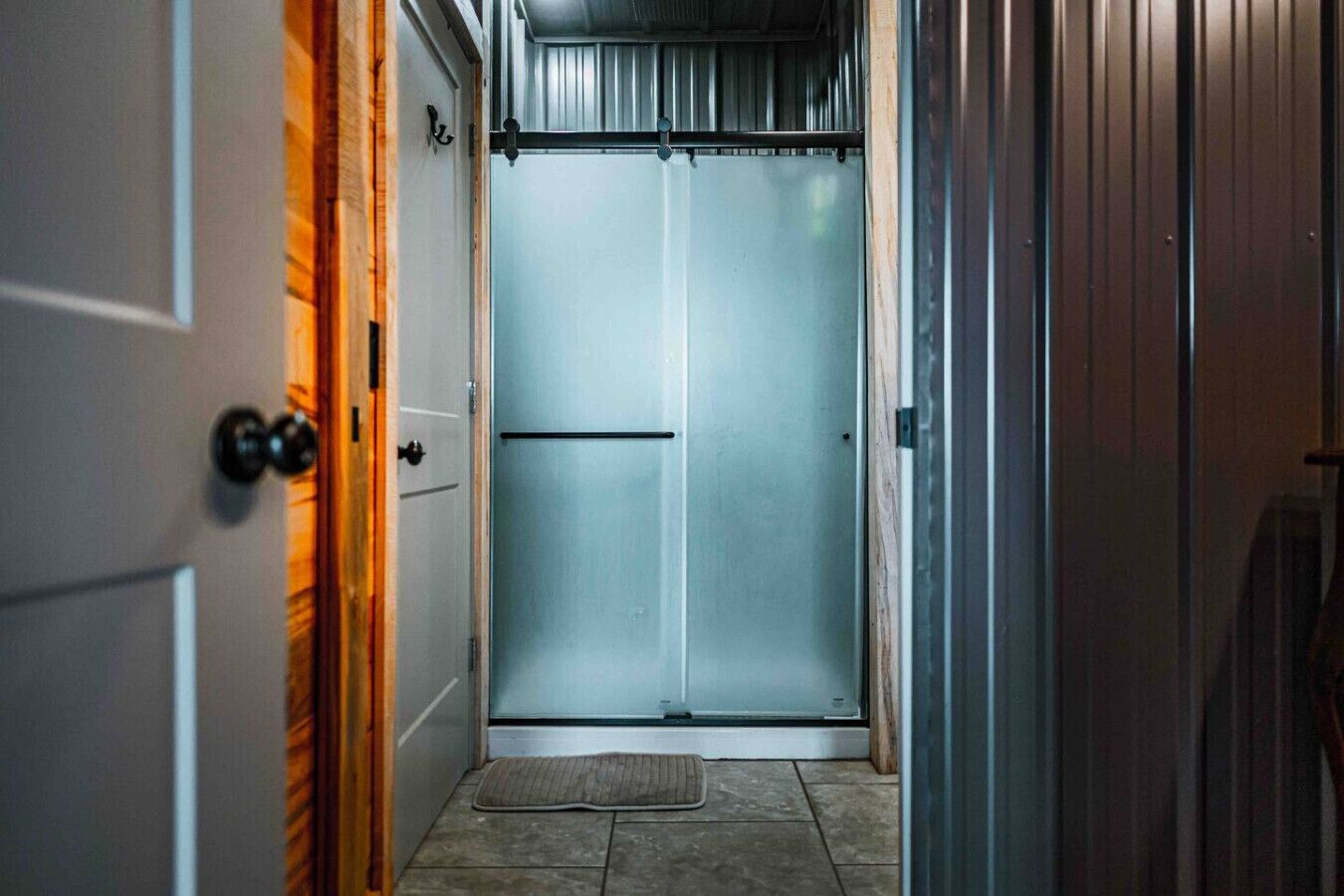 A narrow hallway with a door at the end leading to a room.