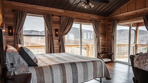 A wooden cabin bedroom with a large bed, a chair, and a view of the outdoors.