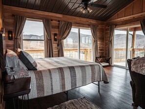 Une chambre dans une cabane en bois, avec un grand lit, une chaise et une vue sur l’extérieur.