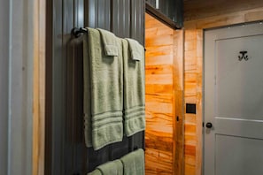 A bathroom with wooden walls, a towel rack with two towels, and a door with a symbol. - Private Cabin & Views@GraysonHighlands (Grayson County)