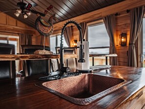 A wooden bar area with a copper sink, a decorative rooster, and a vintage-style light fixture.
