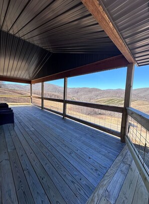 A covered wooden deck with a view of a mountainous landscape.