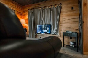Une pièce avec un intérieur en bois, un téléviseur diffusant des services de streaming, un bureau avec une lampe et une chaise.