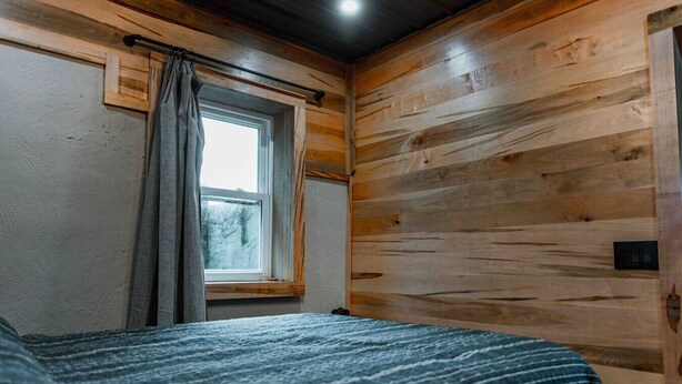 A room with wooden walls, a window with curtains, and a bed with a striped blanket.