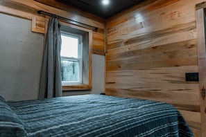 A room with wooden walls, a window with curtains, and a bed with a striped blanket.