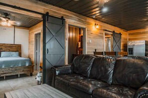 A cozy cabin interior with a bed, leather sofa, and a kitchen area.