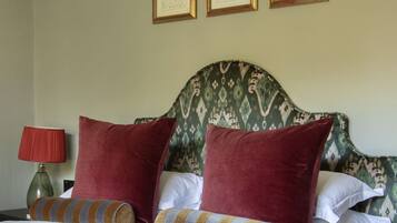 A neatly made bed with red and striped pillows, a green patterned headboard, and three framed botanical prints on the wall.