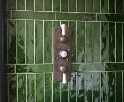 Un baño con paredes cubiertas de azulejos verdes y un interruptor de luz instalado en la pared.
