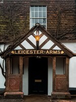 Un edificio con un letrero que dice 'LEICESTER ARMS' sobre una entrada oscura.