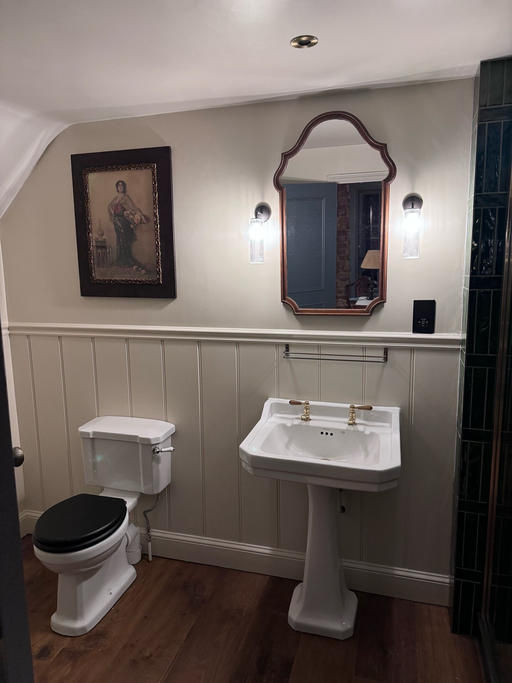 Une salle de bain équipée de toilettes, d’un lavabo, d’un miroir et de luminaires fixés au mur.