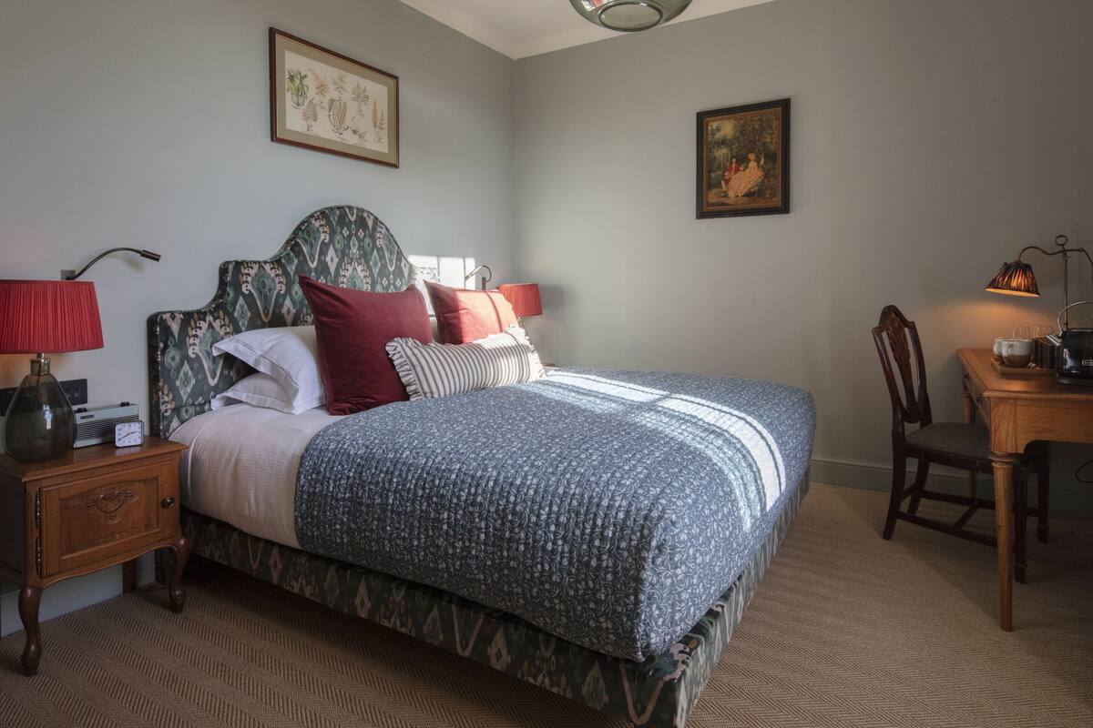 A neatly arranged bedroom with a bed, bedside table, lamp, and a chair.