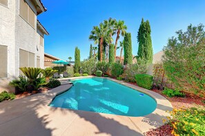 Una piscina circondata da un giardino curato con palme e cipressi.