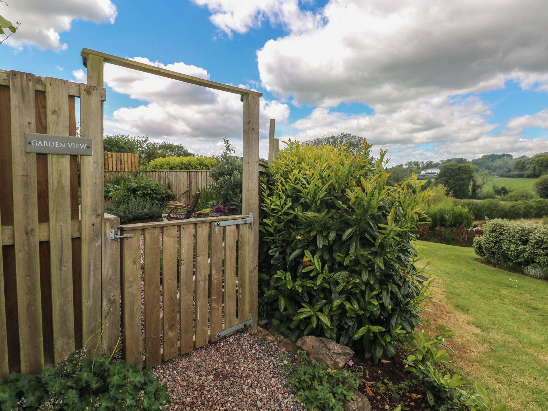Una verja de madera con un letrero que dice 'GARDEN VIEW' da acceso a un jardín bien cuidado.