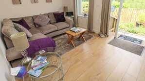 A living room with a sofa, a coffee table, and a glass table with magazines. There is a window with curtains and a view of greenery outside. - Garden View (Pembroke)