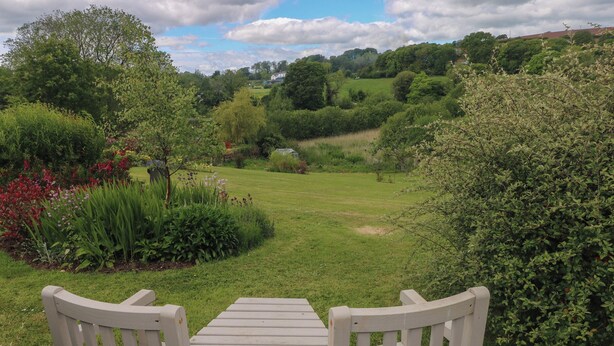 A garden with a table and chairs, surrounded by greenery and a view of the countryside. - Garden View (Pembroke)