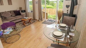 A modern living room with a glass dining table set for two, a sofa, a coffee table, and a view of a garden through large sliding doors. - Garden View (Pembroke)