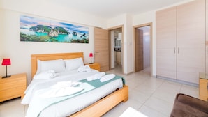 A hotel room with a bed, a nightstand with a lamp, a wardrobe, and a painting of a coastal landscape.