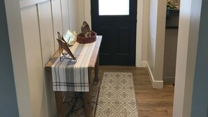 A hallway with a wooden bench, a patterned rug, a black door, and a wall with framed pictures.