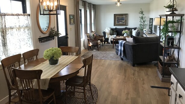 A dining area with a wooden table, chairs, and a chandelier. There is a living room with a sofa and a coffee table.