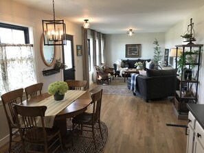 A dining area with a wooden table, chairs, and a chandelier. There is a living room with a sofa and a coffee table. - Prairie View Cottage! New backyard deck at private and cozy country retreat! (Janesville)