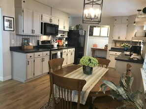 Una cocina moderna con armarios blancos, un refrigerador negro, un microondas y un comedor con una mesa y sillas de madera.