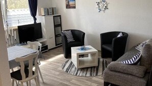 Un salon moderne avec un coin repas, comprenant un téléviseur à écran plat, deux fauteuils, un canapé et une petite table basse.