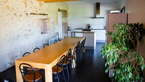 Een eethoek met een lange houten tafel en stoelen, een bakstenen muur en een keuken op de achtergrond.