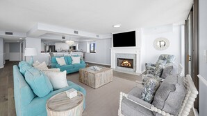 A modern living room with a fireplace, a kitchen in the background, and a large TV mounted above the fireplace. - Penthouse, 180° View, Lazy River, Hot Tub, Sleeps 12 (North Myrtle Beach)