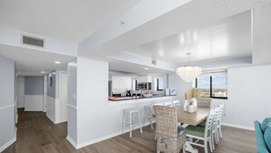 A modern kitchen with white cabinetry, a wooden dining table, and a view of the city. - Penthouse, 180° View, Lazy River, Hot Tub, Sleeps 12 (North Myrtle Beach)