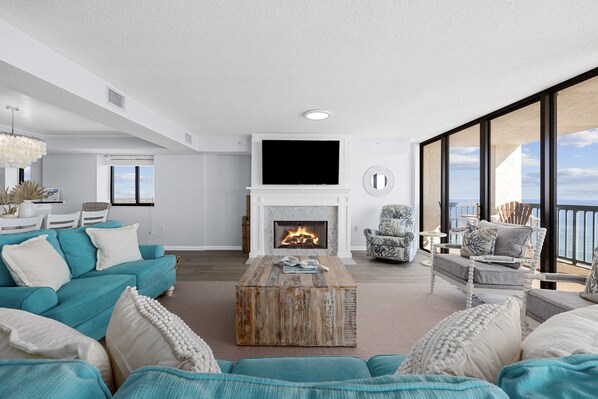 Een moderne woonkamer met een open haard, een grote televisie en een balkon met uitzicht op zee.