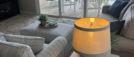 Un salón con sofá, una mesa de centro y una lámpara. Se ve una ventana grande con vistas a una piscina y edificios.