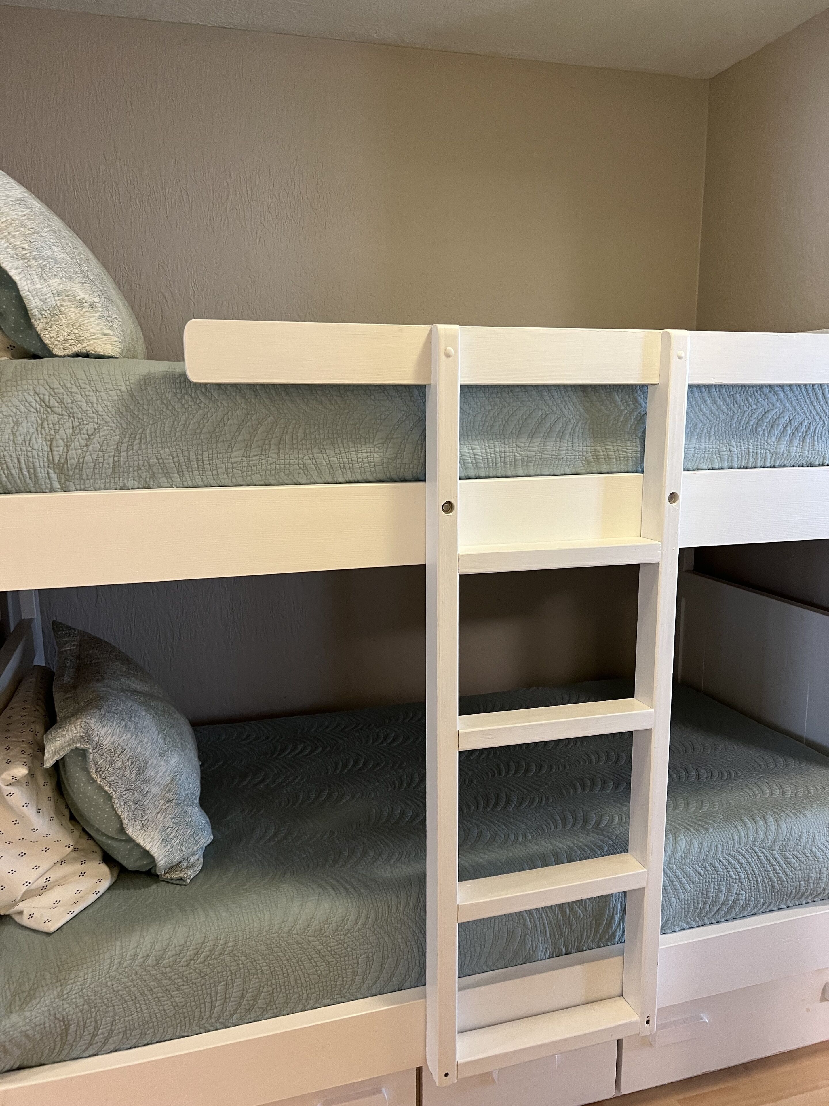 A bunk bed with a ladder, two pillows, and a green mattress.
