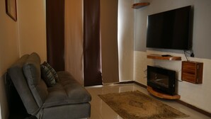 Ein Wohnzimmer mit einer Couch, einem flachbildfernseher an der Wand, einem Holz-TV-Möbel und einem Kamin.