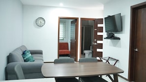 Una sala de estar moderna con un sofá gris, una mesa de comedor de madera y un televisor montado en la pared.