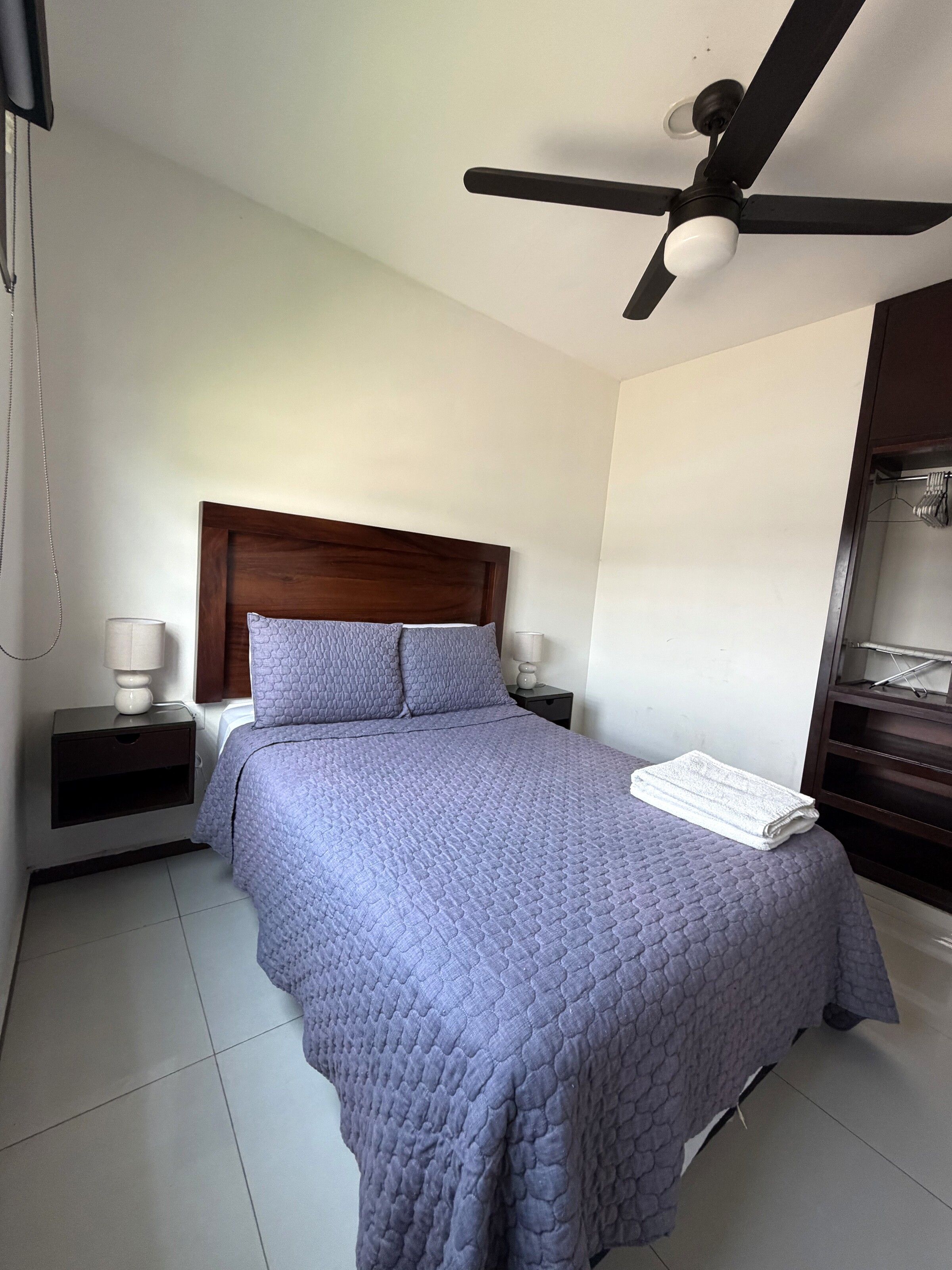 Un dormitorio con cama, mesita de noche, ventilador de techo y armario.