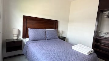 Un dormitorio con cama, mesita de noche, ventilador de techo y armario.