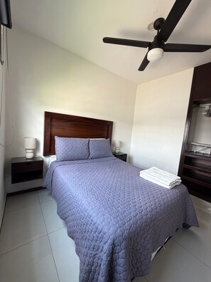 A bedroom with a bed, a nightstand, a ceiling fan, and a wardrobe.