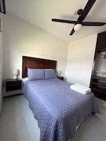 Un dormitorio con cama, mesita de noche, ventilador de techo y armario.