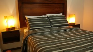 Ein ordentlich bezogenes Bett mit gestreifter Bettwäsche und zwei Nachttischlampen.