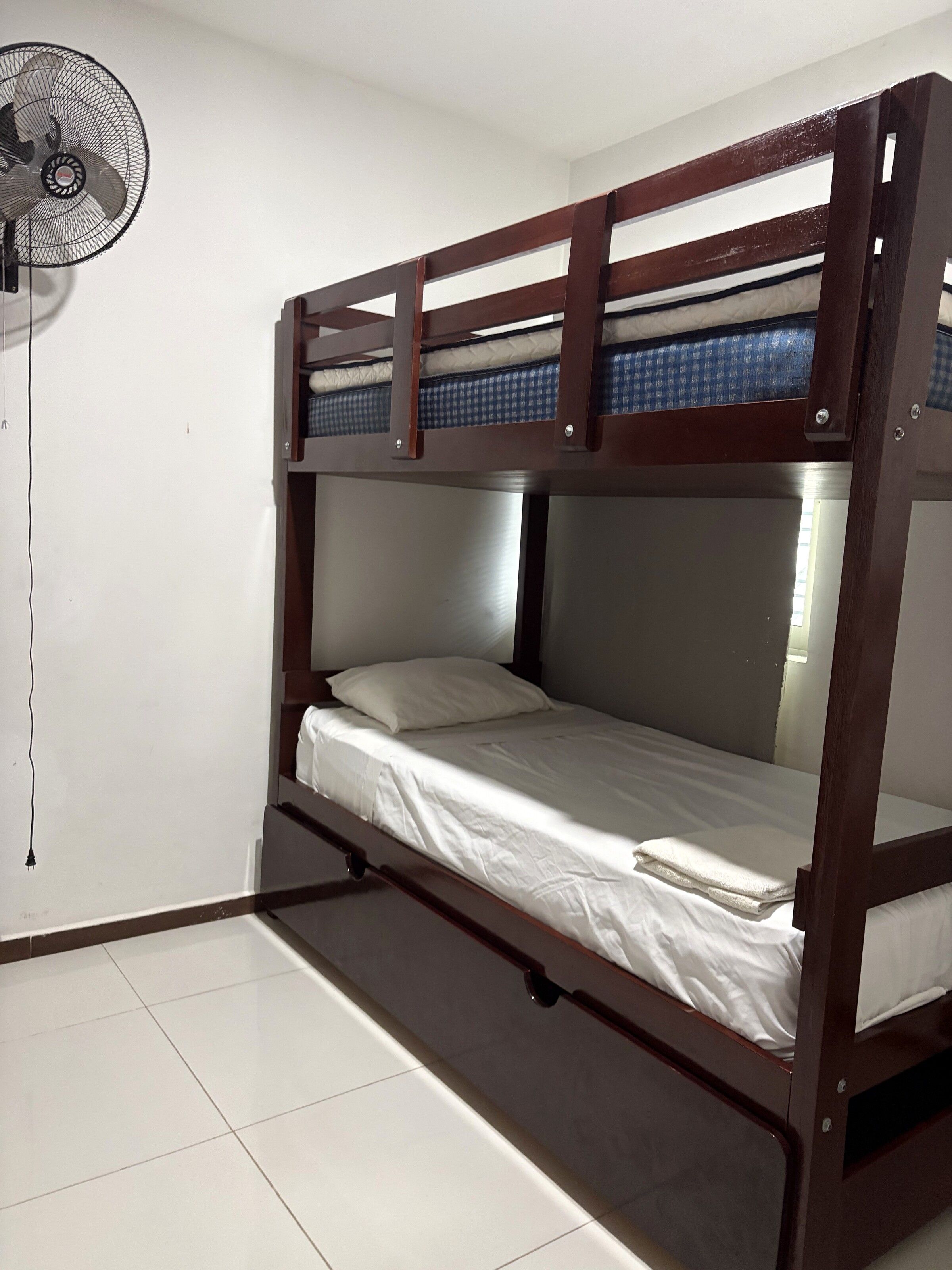 A bunk bed with a fan on the left, white bedding, and a tiled floor.