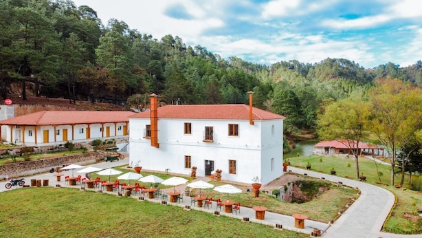 A white building with a red roof, surrounded by a garden and outdoor seating area.
